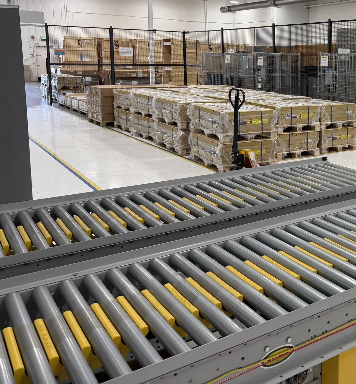 Pallets of GPU servers in caged bonded storage beside roller conveyors
